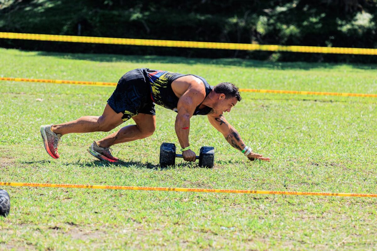 Athlete competing outdoors using dumbbells on a green field in a fitness competition.
