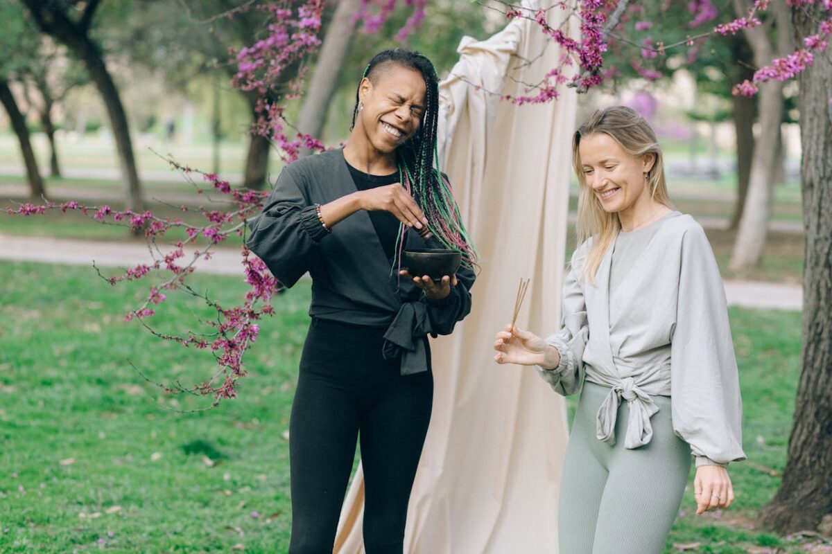 Two women enjoying aromatherapy amidst blooming trees in a serene outdoor park setting.